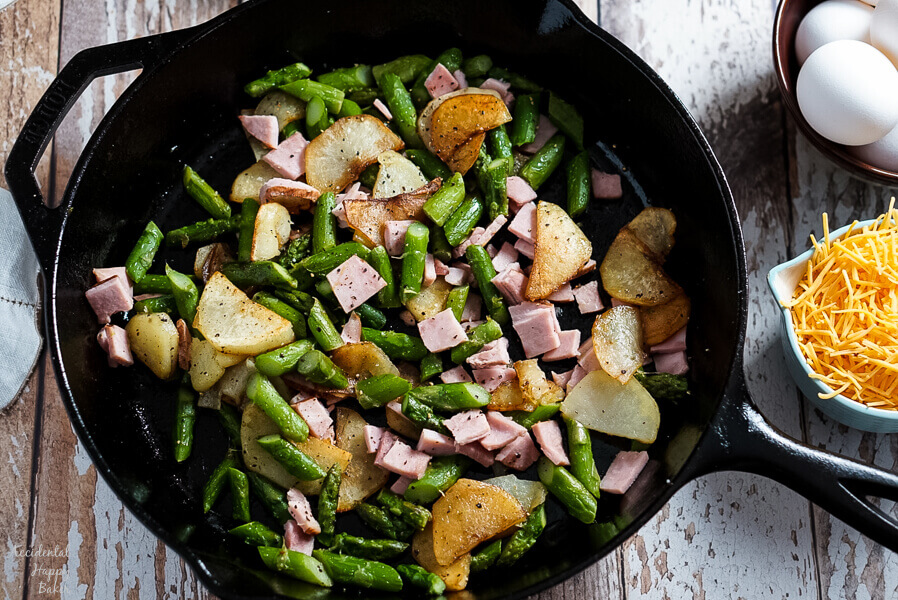 Potatoes, Ham, and Asparagus are cooked in a cast iron skillet before adding the eggs.