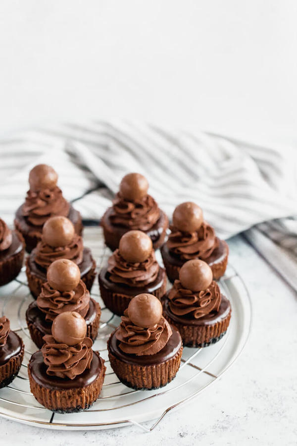 Chocolate Lovers Unite! These Mini Triple Chocolate Cheesecakes are an insanely decadent treat perfect for the ultimate chocolate lover! A rich and creamy chocolate cheesecake sits on top of an Oreo crust. It’s then topped with chocolate whipped cream, chocolate ganache and chocolate shavings! | queensleeappetit.com #chocolate #ganache #dessert #easy #sweet #chocolatecheesecake #cheesecake mini chocolate cheesecakes made with an Oreo crust and topped with dark chocolate ganache, chocolate whipped cream and chocolate truffles.